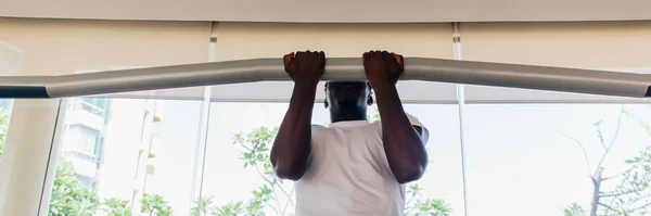 Forte sportivo afroamericano in t-shirt bianca che fa pull up durante l'allenamento di fitness in palestra moderna — Foto Stock
