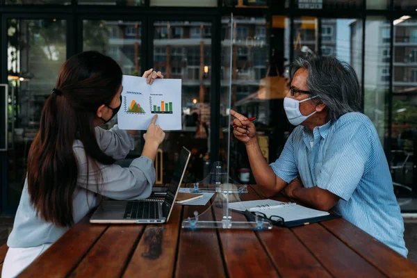 Asyalı iş adamı ve kadın kahve dükkanında maske takarak tartışıyorlar.