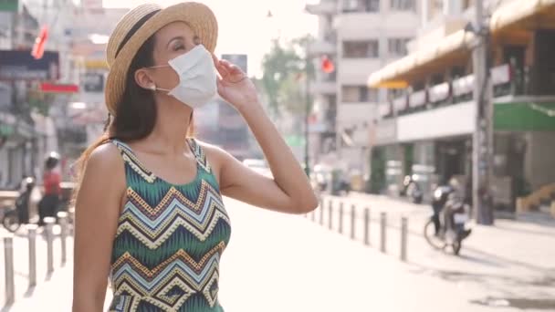 タイのバンコクを旅行している若いブルネットの女性は、パンデミックコロナウイルスの間に人気のあるカオサン道路で。20代ヒスパニックで保護マスク着用夏ノースリーブ夏のドレスでアジア — ストック動画