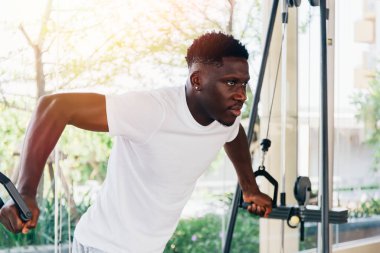 Spor salonunda idman sırasında pencerenin önünde duran spor makinesiyle kablo uçuşu yapan kaslı Afrikalı Amerikalı sporcu.