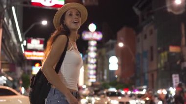 Genç esmer kadın yalnız gezgin yaz kıyafetleriyle akşam vakti şehir caddesinde yürüyor.