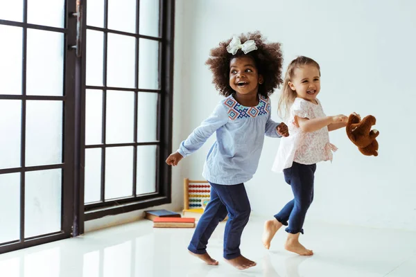 Candid portrait of two energetic playful young diverse friends children playing indoors — Stock Photo, Image