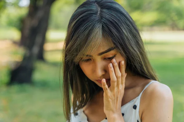 Молодая брюнетка плачет и вытирает слезы в парке. Красивая девушка несчастна и печальна на открытом воздухе — стоковое фото