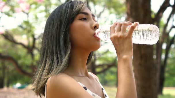 Joven morena bebiendo agua en el parque. Hermosa chica asiática sedienta y tomando un sorbo de agua al aire libre — Vídeos de Stock