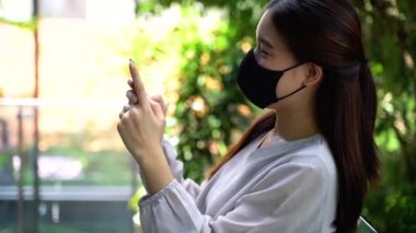 Ofisteki akıllı telefonu kullanarak yüz koruması için cerrahi maskeli güzel bir Asyalı kadın.