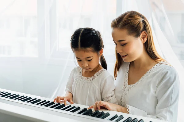 Азійська мати вчить дочку грати на клавіатурі. — стокове фото