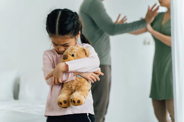 Młoda Chinka przytula Teddy 'ego z rodzicami kłócącymi się — Zdjęcie stockowe