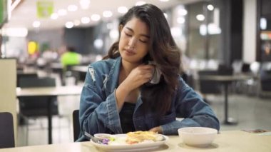 Kafeteryada oturan genç Asyalı kadın koruyucu yüz maskesi takmış kameraya bakıyor. Cafe restoranında oturan güzel Asyalı kız.