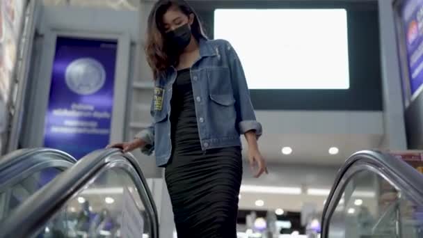 शॉपिंग मॉलमध्ये एस्केलेटर खाली येत संरक्षक चेहरा परिधान तरुण आशियाई स्त्री — स्टॉक व्हिडिओ