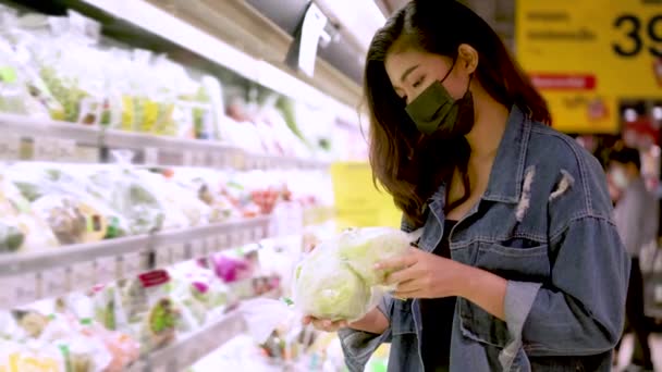 Молодая азиатка с защитным лицом выбирает еду в супермаркете — стоковое видео