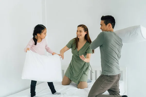Joven familia asiática jugando con almohadas en la cama —  Fotos de Stock