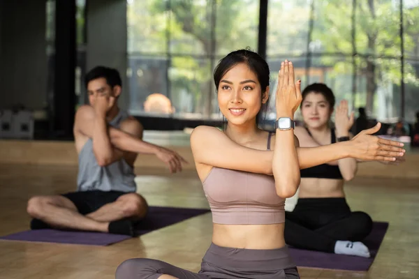 Gruppe asiatischer Mädchen in Yoga-Stretching-Position im Aerobic-Fitnesskurs im Fitnessstudio. Glückliche junge Sportler mit überkreuzten Beinen auf der Yogamatte. — Stockfoto