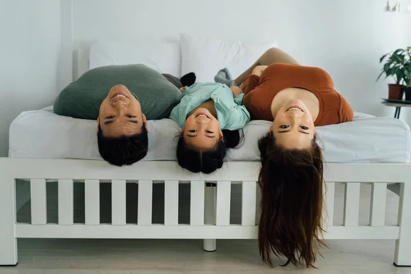 Portrait of young Asian family lying upside down on bed — Stock Photo, Image