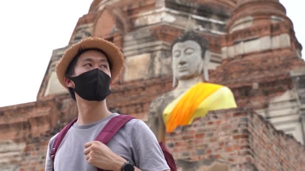 Asiatisk man ler bakom den svarta masken när han reser till Ayutthaya, Thailand. Bär en skyddande mask för att förhindra från coronavirus Covid-19 — Stockvideo