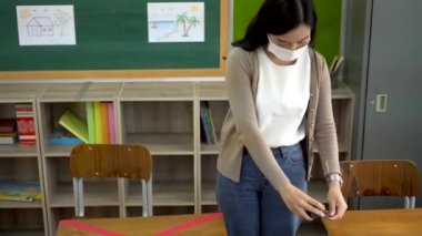 Yüz maskesi takan Asyalı bayan öğretmen ilkokulda sınıflar arasındaki mesafeyi ölçer. Covid19 yeni normal kavram için eğitim yapılanmasında sosyal uzaklık politikası