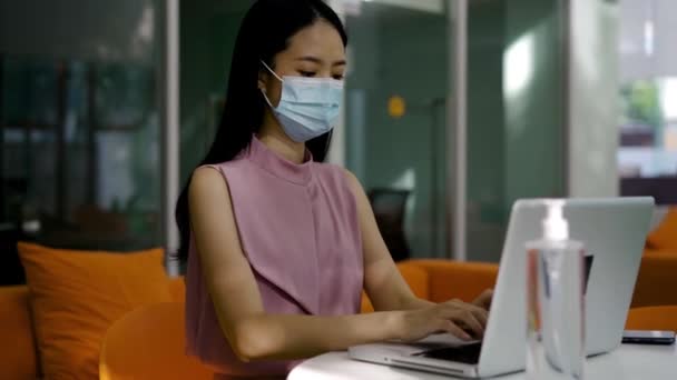 Mujer de negocios asiática con protección Covid-19 mascarilla que trabaja en la oficina moderna, utilizando la computadora, concentración, protección, salud - nueva vida laboral normal — Vídeo de stock