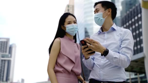 Hombre de negocios y mujer asiáticos con máscara facial mirando el teléfono celular en el entorno urbano, la vida en la ciudad, la pandemia, la vida laboral, colega - Covid19 pandemia — Vídeos de Stock