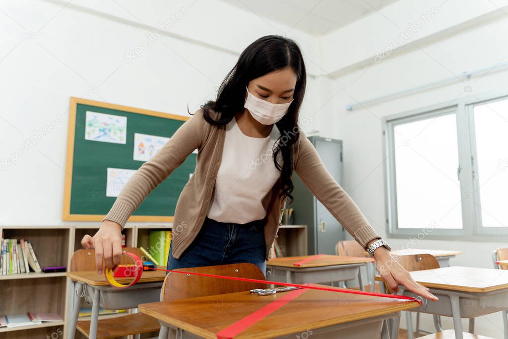 Female teacher using a red tape on the desks in classroom in primary school to keep social distancing measure policy in education building for Covid19 new normal concept