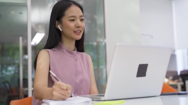 Fröhliche asiatische Geschäftsfrau auf Videoanruf mit Kollegen, trägt Kopfhörer im modernen Büro, Glück, Existenzgründung, Unternehmer — Stockvideo
