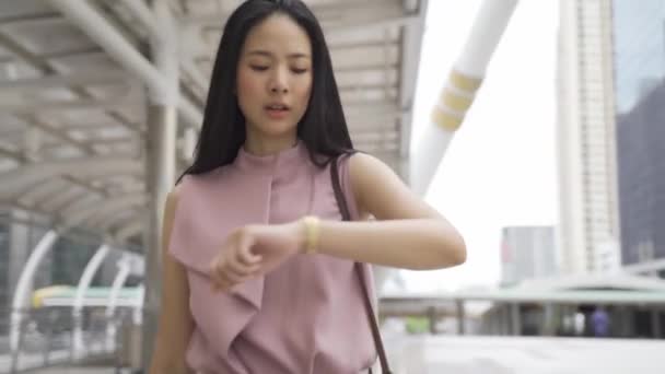 Молода азіатська бізнесменка дивиться на годинник і швидко йде біля офісного будинку. Приваблива бізнес-дівчина Азії поспішає і поспішає на зустріч. Китайська корейка запізнюється на роботу. — стокове відео