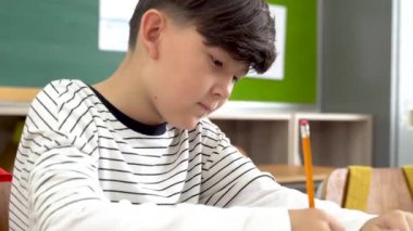 Sınıfta masa başında oturan erkek öğrenci sınavda not defterine yazıyor.