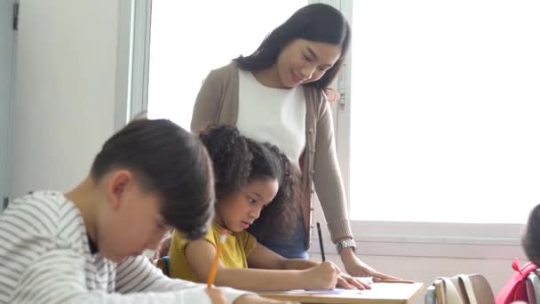 Aziatische leraar assisteren studenten in de klas. Jonge vrouw werkt op school helpen jongen met zijn schrijven, onderwijs, ondersteuning, zorg — Stockvideo