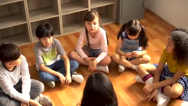 Grupo multiétnico de escolares sentados en el suelo escuchando al maestro de escuela asiático — Vídeo de stock