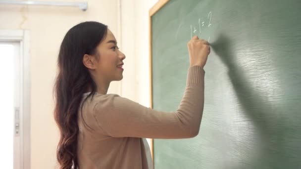 Jong vrouwelijk aziatisch leraar schrijven wiskunde sommen op schoolbord — Stockvideo