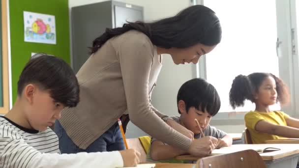 아시아 학교 선생님 이 교실에서 학생들을 돕고 있습니다. 학교에서 일하는 젊은 여자가 남자 아이의 글쓰기, 교육, 지원, 보살핌을 도와 주고 있습니다. — 비디오