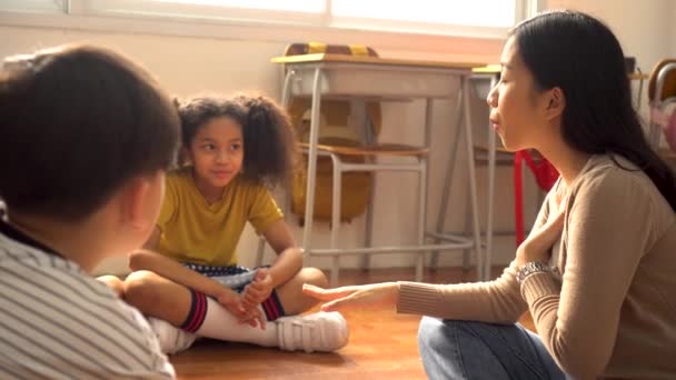 Grupo multiétnico de escolares sentados en el suelo escuchando al maestro de escuela asiático — Vídeo de stock