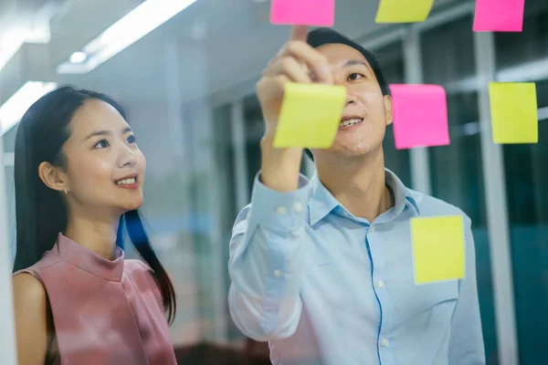 Compañeros de negocios asiáticos usando notas adhesivas en ventana — Foto de Stock