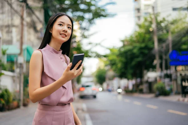 Cheerful Asian businesswoman using phone and waiting for taxi — Stock Photo, Image