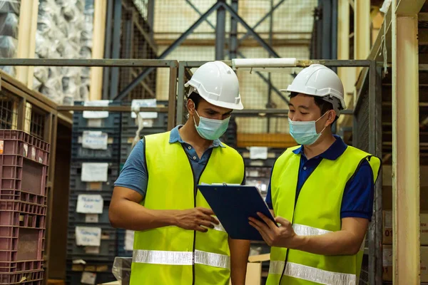 Group of young factory warehouse workers wearing a protective face mask while working in logistic industry. Asian and Indian ethnic men checking item stock order during Covid 19 pandemic — Stock Photo, Image