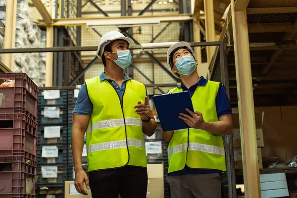 Group of young factory warehouse workers wearing a protective face mask while working in logistic industry. Asian and Indian ethnic men checking item stock order during Covid 19 pandemic — Stock Photo, Image