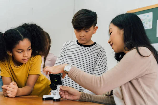 Asian school teacher helping students use microscope — Stock Photo, Image