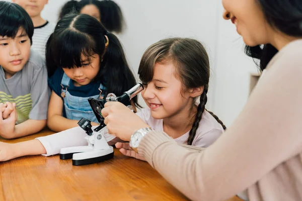Asian school teacher helping students use microscope