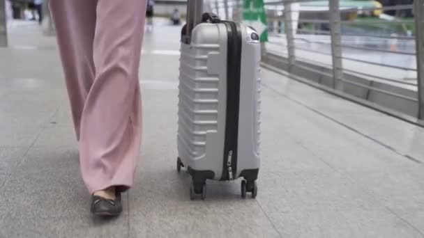 Pies de vista frontal de mujer de negocios caminando mientras arrastra una bolsa de carro en edificios urbanos modernos. Viajeros femeninos que viajan por negocios. — Vídeo de stock