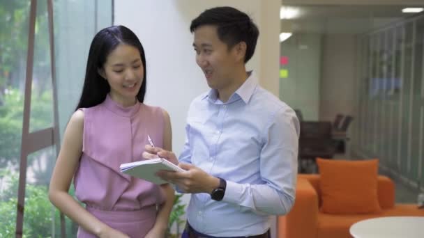 Asian businessman and woman smiling and working together, writing in notebook, collaboration, cooperation, teamwork — Stock Video
