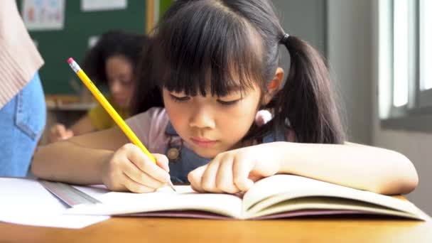 Niña de la escuela sentada en la escuela escribiendo en libro con lápiz, estudiando, educación, aprendizaje. Niños asiáticos en la clase. Diversidad estudiantil — Vídeos de Stock