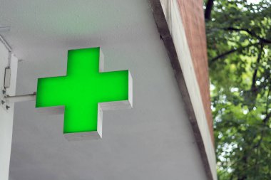 Neon yeşil eczane çapraz, bir bokeh bina ve ağaçlar arka plan altında