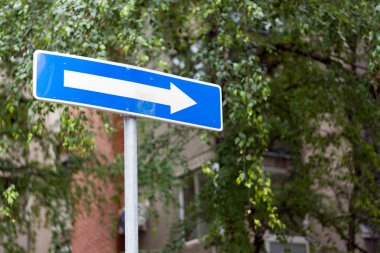 Sağ yön gri binalar ve bulutlu gökyüzü bokeh arka plan karşı, bir şehir caddesi üzerinde tek yönlü mavi sokak işareti izin
