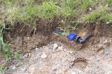 Yeşil çim yüzeyinin altındaki toprakta görülebilen siyah ve mavi tesisat borusu