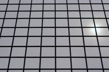 Siyah metal ağ çit, gri bulutlu gökyüzüne karşı, güneş gizleme