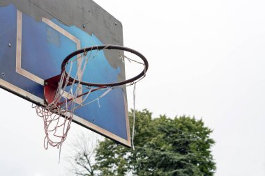 Yırtık eski basketbol potası, gri bulutlu gökyüzüne karşı halka açık bir parkta, mavi tahta kapalı kapalı bir grungy üzerinde