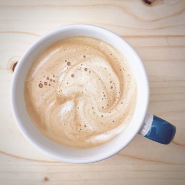 Ahşap masada köpüklü Latte yakın beyaz ve mavi kahve bardağı