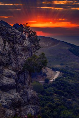 Vibrant sunset over the mountains of Samothrace Island in Greece with a road in the background and cliffs in the foreground clipart