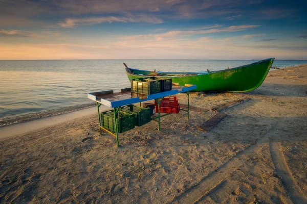 Wooden table used by the fishermen to sort the fish before selling it when they arrive from fishing with crates on and under the table and a wooden boat on the Black Sea Coast in Romania at Corbu, Constanta County