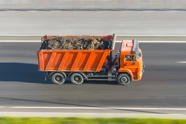 Truck dump with a load of soil in the body rides at high speed on the highway