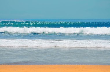 Deniz kumlu Sahili küçük dalgalar, bulutların üstünde bir yaz gününde mavi bir gökyüzü mavi su ile