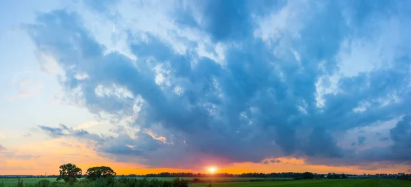 Panorama of rural landscape, sky in dark clouds dramatic bright sunset